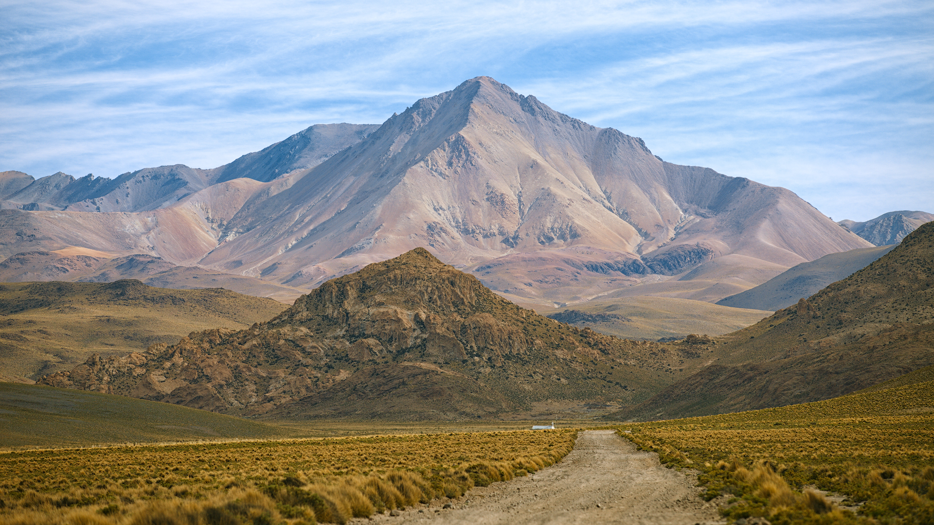 This captivating image leads the viewer along a dusty trail towards the soaring peaks of the Bolivian Andes. The mountain&rsquo;s stratified colors from mineral deposits create a stunning visual gradient, contrasting with the rough textures of the surrounding landscape. The road, a symbol of adventure, invites one to explore the untamed beauty of Bolivia&rsquo;s high-altitude wilderness.