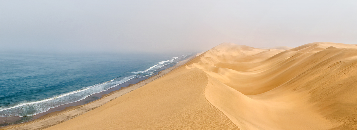 This image beautifully contrasts the sweeping golden dunes of the desert with the serene blue of the ocean. The scene where these two vast and differing landscapes converge is captured here, symbolizing the natural world&rsquo;s diverse beauty and the harmonious coexistence of contrasting elements.